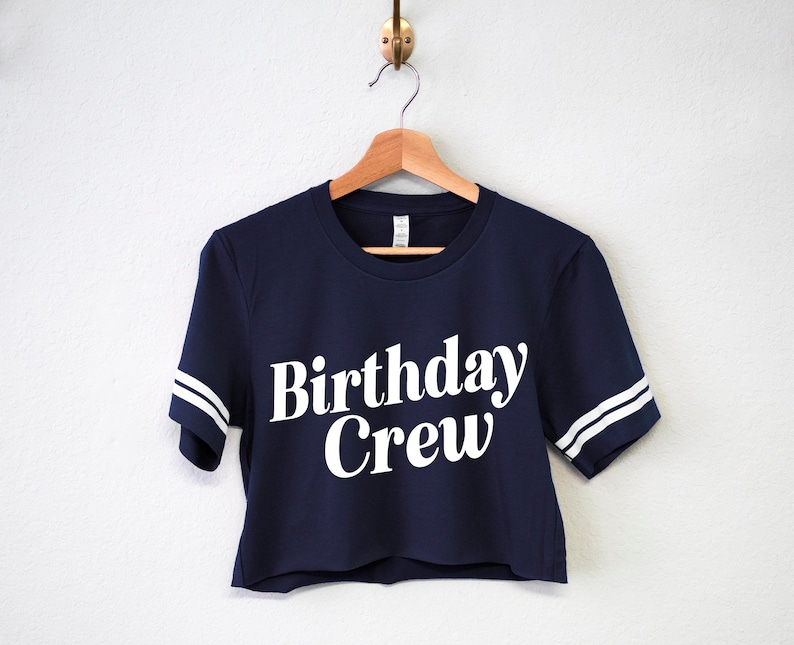 May include: A navy blue cropped t-shirt with white stripes on the sleeves and the text "Birthday Crew" in white.