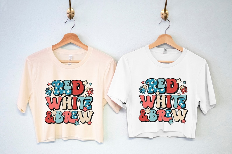May include: Two cropped t-shirts with a red, white, and blue graphic that says "Red White & Brew" with stars and beer mugs. The shirts are on hangers against a light blue wall.