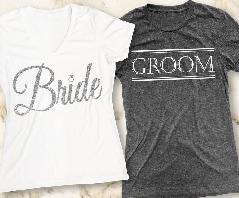 Puede incluir: Dos camisetas blancas con las palabras "Bride" y "Groom" impresas en ellas. La camiseta de la novia tiene un dise&ntilde;o de purpurina plateada y la camiseta del novio tiene un contorno blanco.