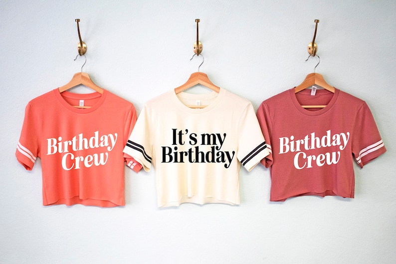 May include: Three cropped t-shirts with white text on different colored shirts. The shirts have black and white stripes on the sleeves. The text on the shirts reads "Birthday Crew", "It's my Birthday", and "Birthday Crew".
