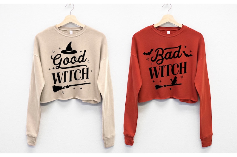 May include: Two cropped sweatshirts with long sleeves. One is beige with the text "Good Witch" and a witch's hat graphic. The other is red with the text "Bad Witch" and a black cat graphic.