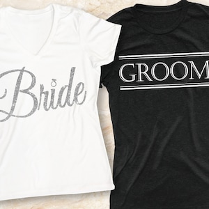 Puede incluir: Dos camisetas blancas con las palabras "Bride" y "Groom" impresas en ellas. La camiseta "Bride" tiene un dise&ntilde;o de purpurina plateada. La camiseta "Groom" tiene un borde de doble l&iacute;nea alrededor de la palabra.