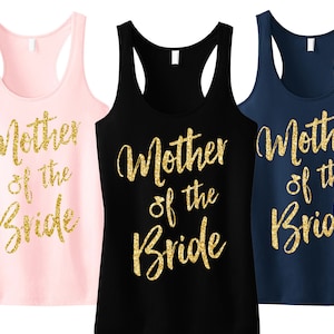 Op de afbeelding: Drie racerback tanktops in roze, zwart en marineblauw. Elke tanktop heeft de gouden glittertekst "Mother of the Bride". De tekst is in een cursief lettertype. De tanktops zijn mouwloos.