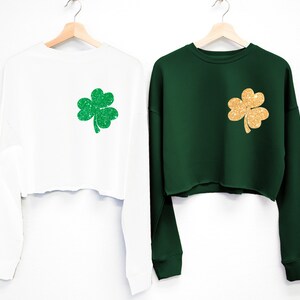May include: Two long-sleeved cropped sweatshirts with a shamrock design. One sweatshirt is white with a green shamrock, and the other is green with a gold shamrock.