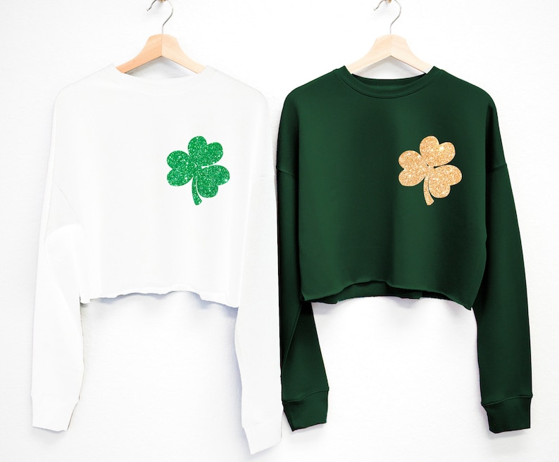 May include: Two long-sleeved cropped sweatshirts with a shamrock design. One sweatshirt is white with a green shamrock, and the other is green with a gold shamrock.