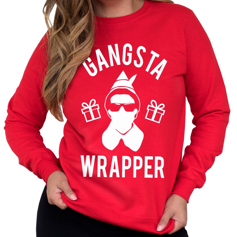 May include: Red Christmas sweater with a white graphic of an elf wearing sunglasses and a face mask. The text "Gangsta Wrapper" is printed on the sweater.