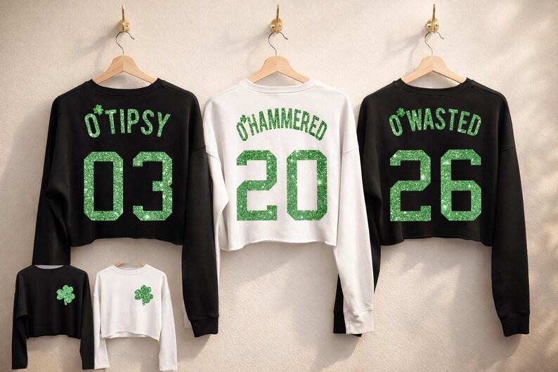 Three cropped St Patrick’s Day sweatshirts hanging on wooden hangers, featuring green glitter print “O’TIPSY 03,” “O’HAMMERED 20,” and “O’WASTED 26” designs on black and white cropped crewneck tops, festive Irish shamrock style women’s holiday apparel.