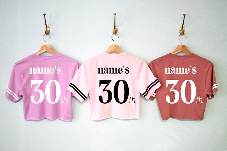 May include: Three pink and red cropped t-shirts with black and white striped sleeves. The shirts have "name's 30th" printed on the back.