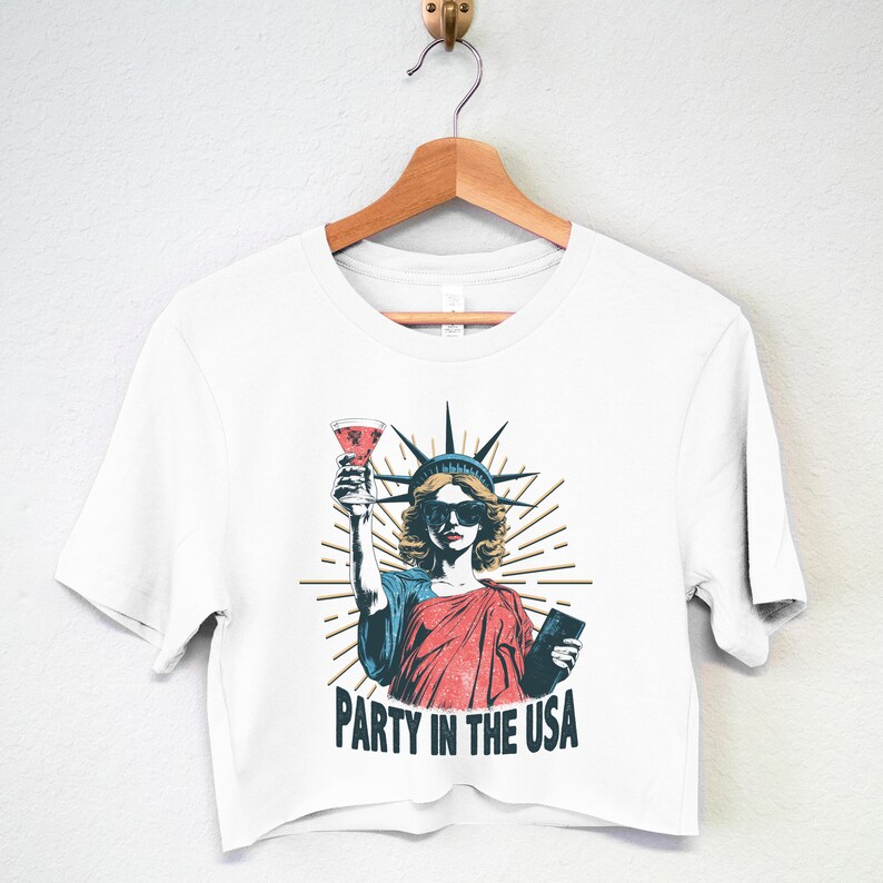 May include: White cropped t-shirt with a graphic of the Statue of Liberty holding a glass of wine and a passport. The text "Party in the USA" is printed below the graphic.
