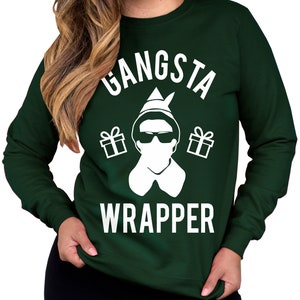 May include: A green sweatshirt with a white graphic of an elf wearing sunglasses and holding gifts. The text "Gangsta Wrapper" is printed on the sweatshirt.