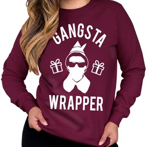 May include: Burgundy sweatshirt with a white graphic of an elf wearing sunglasses and a Santa hat. The graphic says "Gangsta Wrapper" with gift boxes on either side of the elf.