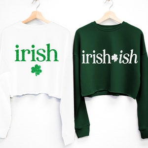 May include: Two white long-sleeved cropped sweatshirts with green shamrock designs. One sweatshirt says "irish" and the other says "irish*ish".