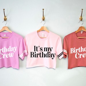 May include: Three pink and red cropped t-shirts with white and black lettering. The shirts say "Birthday Crew" and "It's my Birthday".