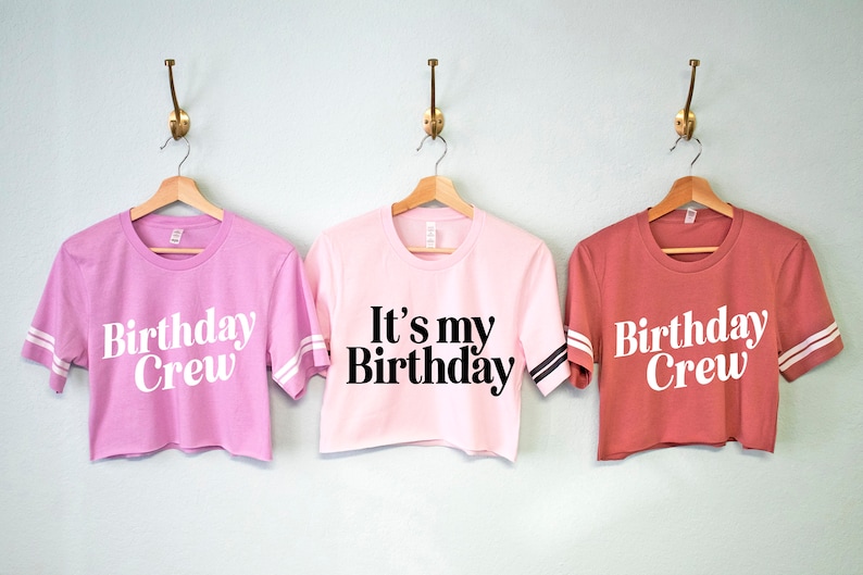 May include: Three pink and red cropped t-shirts with white and black lettering. The shirts say "Birthday Crew" and "It's my Birthday".