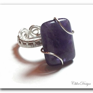 May include: A silver wire wrapped ring with a rectangular amethyst gemstone. The ring is set on a white background.