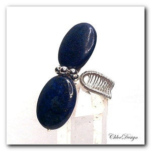 May include: A silver wire wrapped ring featuring two oval shaped lapis lazuli stones. The ring is displayed against a white background.