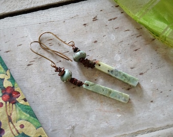 Peut inclure: Une paire de boucles d'oreilles pendantes avec des perles en céramique vertes et brunes et un long pendentif rectangulaire en pierre verte.