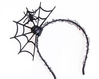 May include: Black headband with a black spider and spiderweb design. The headband is made of lace and has a black bow.