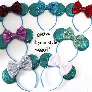 Puede incluir: Seis estilos diferentes de diademas con orejas color turquesa y lazos de varios colores. Los lazos están hechos de lentejuelas y son de color rojo, rosa, morado, azul claro, plateado y blanco. El texto "Pick your style" está impreso debajo de las diademas.