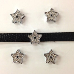 May include: Five star-shaped embellishments with clear rhinestones and silver-colored metal frames. One star is attached to a black choker-style necklace. The stars are arranged on a white background.