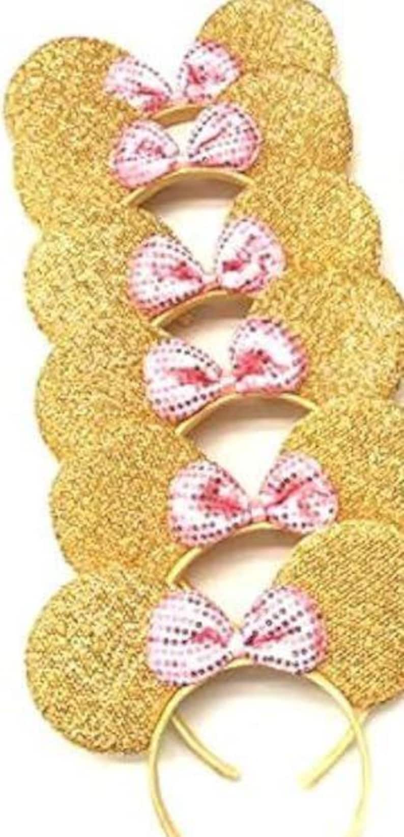 May include: Several gold sequined mouse ear headbands with pink and white polka dot bows. The ears are round and glittery, and the headbands are a thin gold color. The bows are centered on the headband.