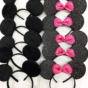 May include: A collection of black mouse ear headbands, some with a plush texture and others with a glittery finish. Several headbands feature bright pink sequined bows, creating a playful and festive look.