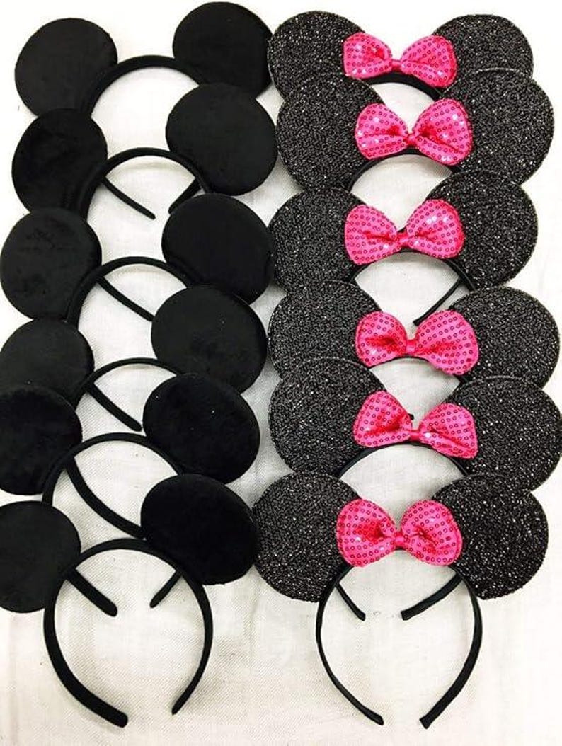 May include: A collection of black mouse ear headbands, some with a plush texture and others with a glittery finish. Several headbands feature bright pink sequined bows, creating a playful and festive look.