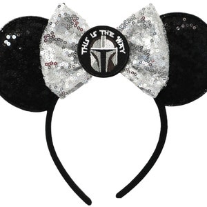 May include: Black and silver sequined Minnie Mouse ears headband with a silver bow and a circular patch featuring a Mandalorian helmet with the text "This is the way".