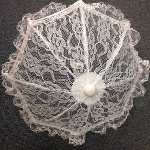 May include: A white lace umbrella with a white plastic handle. The umbrella is closed and has a delicate floral pattern.