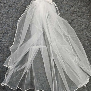 May include: White bridal veil with a beaded tiara attached. The veil is made of soft tulle and has a scalloped edge.