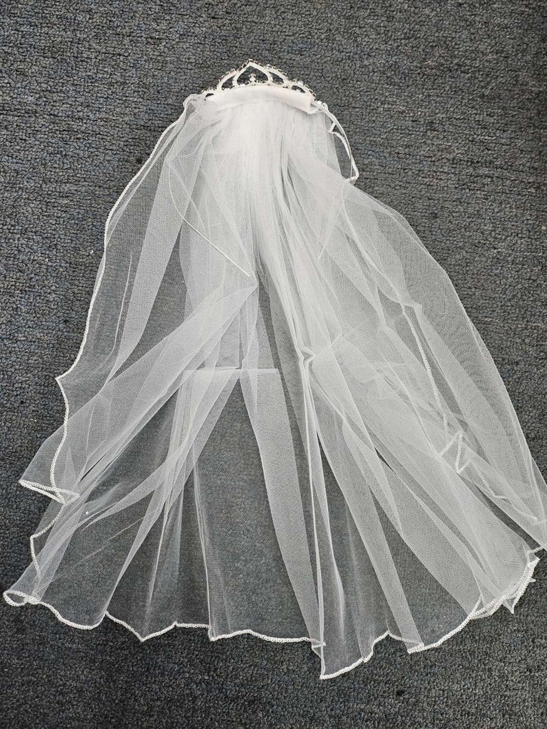 May include: White bridal veil with a beaded tiara attached. The veil is made of soft tulle and has a scalloped edge.