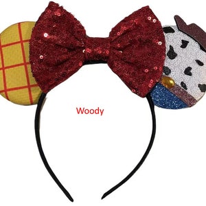 May include: Red sequined bow headband with a yellow and red checkered fabric ear and a white, black, and blue fabric ear with a sheriff's star. The headband says "Woody".