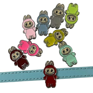 May include: A collection of colorful enamel pins shaped like cartoon bunnies in various colors, including pink, blue, gray, green, yellow, red, and teal. The pins are attached to a light blue strap.