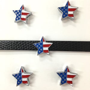May include: Five silver star-shaped charms with an American flag design. The stars are red, white, and blue with a silver outline. The charms are on a white background.