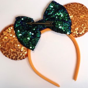 May include: Orange and green sequined Minnie Mouse ears headband with a gold arrow bow.