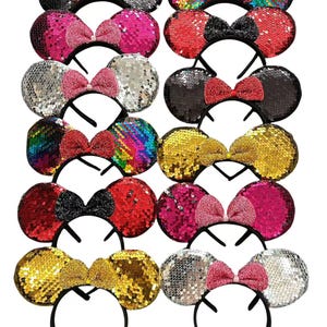May include: A collection of sequined mouse ear headbands in various colors, including black, silver, pink, red, gold, and rainbow. Each headband features a matching bow. The headbands are on a black plastic frame.