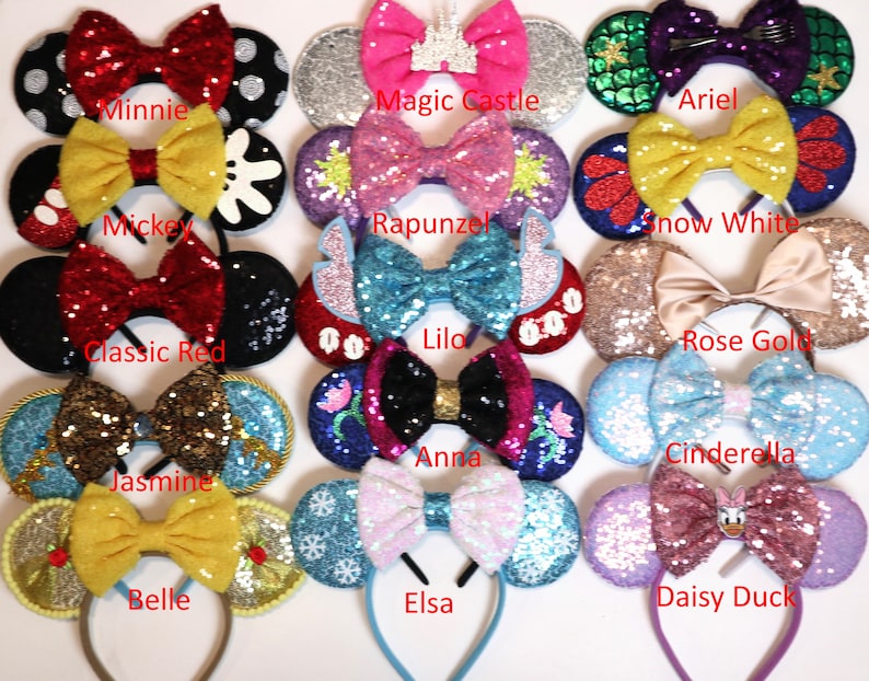 May include: A collection of 12 pairs of Disney character-themed mouse ears with glitter and sequin embellishments. The ears are arranged in three rows of four. Each pair features a different character, including Minnie Mouse, Magic Castle, Ariel, Mickey Mouse, Rapunzel, Snow White, Classic Red, Lilo, Rose Gold, Jasmine, Anna, Cinderella, Belle, Elsa, and Daisy Duck.
