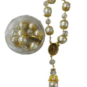 May include: A rosary with large, faux pearl beads and gold-colored accents. The rosary includes a small oval pendant with an image and a decorative angel pendant. A clear plastic container holds additional pearl beads.