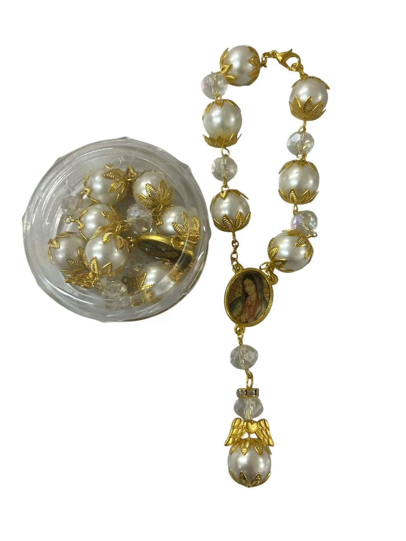 May include: A rosary with large, faux pearl beads and gold-colored accents. The rosary includes a small oval pendant with an image and a decorative angel pendant. A clear plastic container holds additional pearl beads.