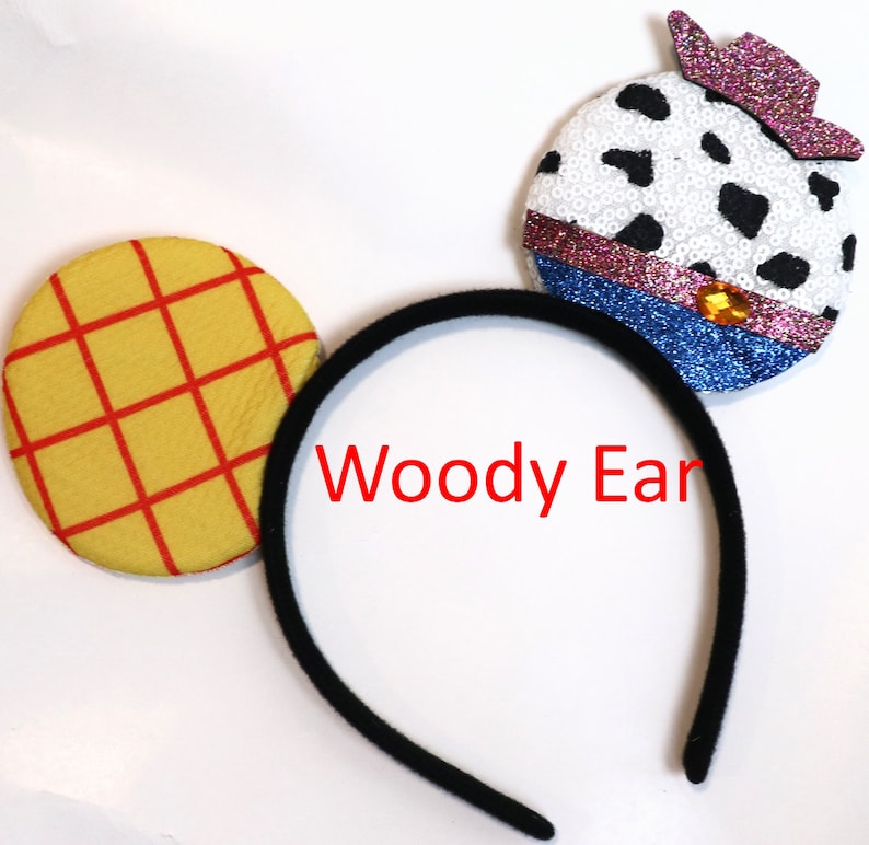 May include: A black headband with two felt ears. One ear is yellow with red squares and the other is white with black spots and a pink and purple cowboy hat. The headband says "Woody Ear".