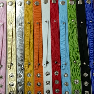 May include: A collection of 14 colorful leather bracelets with silver metal accents. Each bracelet has a unique color and texture, including pink, light pink, gold, silver, yellow, orange, white, red, light blue, green, black, blue, and purple.