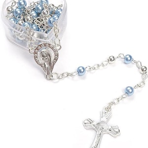 May include: A rosary with light blue and silver beads, a silver crucifix, and a silver Virgin Mary pendant. The beads are stored in a clear, heart-shaped container.