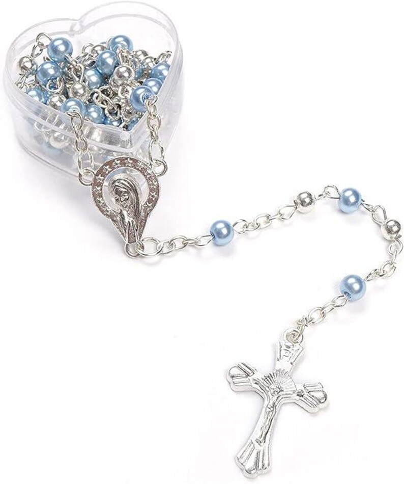 May include: A rosary with light blue and silver beads, a silver crucifix, and a silver Virgin Mary pendant. The beads are stored in a clear, heart-shaped container.