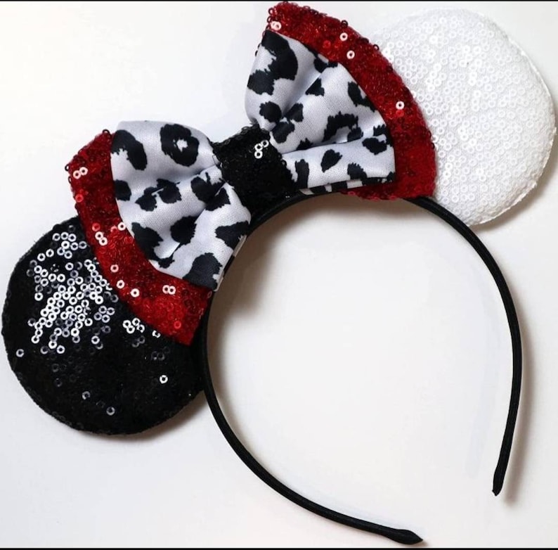 May include: Black and white dalmatian print bow with red sequins on a black headband with black and white sequin ears and a white sequin ear.