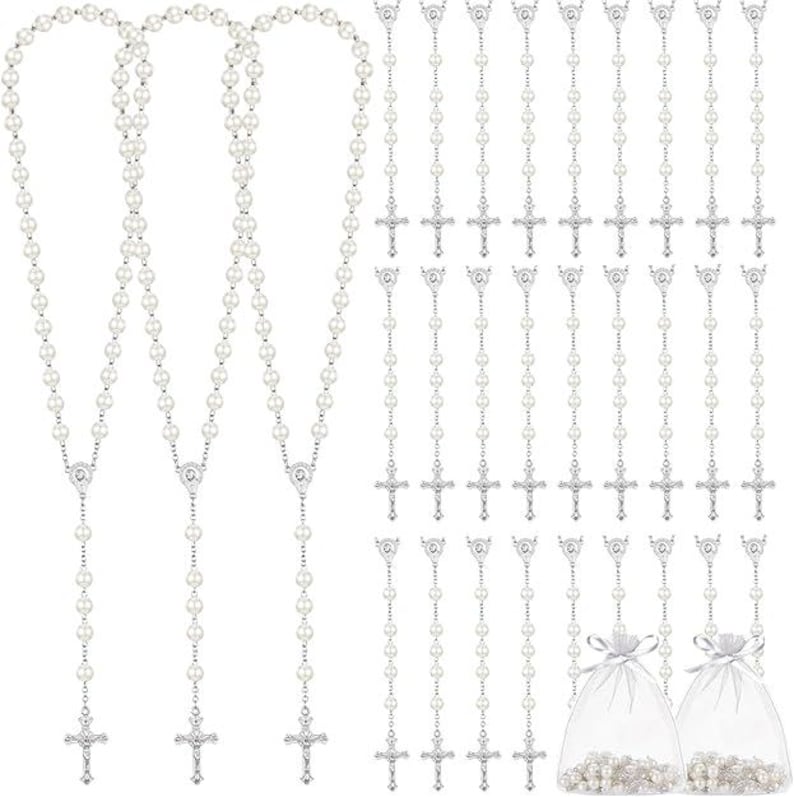 May include: A collection of rosaries featuring faux pearl beads and silver-toned crucifixes. The image includes several long rosary necklaces and individual rosary strands, some packaged in small, sheer drawstring bags. The rosaries are a religious item.