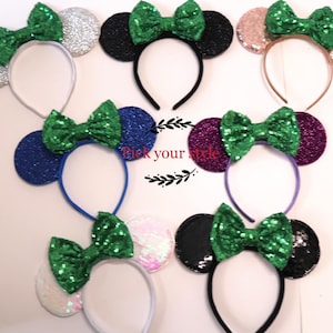 May include: Assortment of colorful sequined Minnie Mouse ears headbands with green bows.  The headbands are available in silver, black, blue, purple, pink, and iridescent.