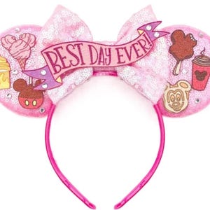 May include: A pink sequined headband featuring two circular ears and a central bow. The bow displays a banner with the text BEST DAY EVER! The ears are decorated with various food-themed icons including ice cream, coffee, and Mickey-shaped treats.