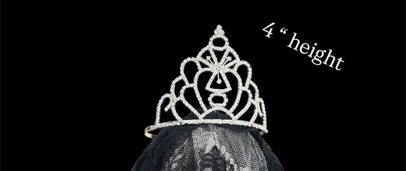 Pode incluir: Uma tiara prateada com strass transparentes, com cerca de 10 cm de altura, assenta sobre um v&eacute;u preto. A tiara apresenta um design vazado com uma forma geom&eacute;trica central e bordas curvas, ideal para casamentos.