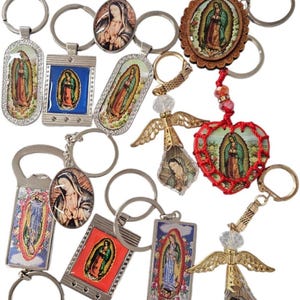 May include: A collection of religious keychains featuring images of the Virgin Mary. The keychains vary in shape and design, including oval, rectangular, and heart-shaped pendants. Some have decorative accents like rhinestones and angel wings.