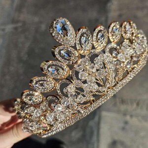May include: A gold crown with clear rhinestones. The crown is made of metal and has a delicate design.